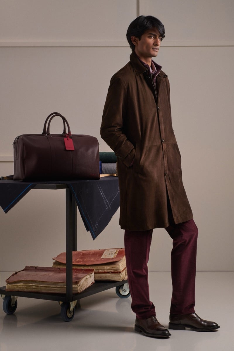 Rishi Robin wears a brown suede car coat over a burgundy shirt with burgundy corduroy trousers and brown leather derbies