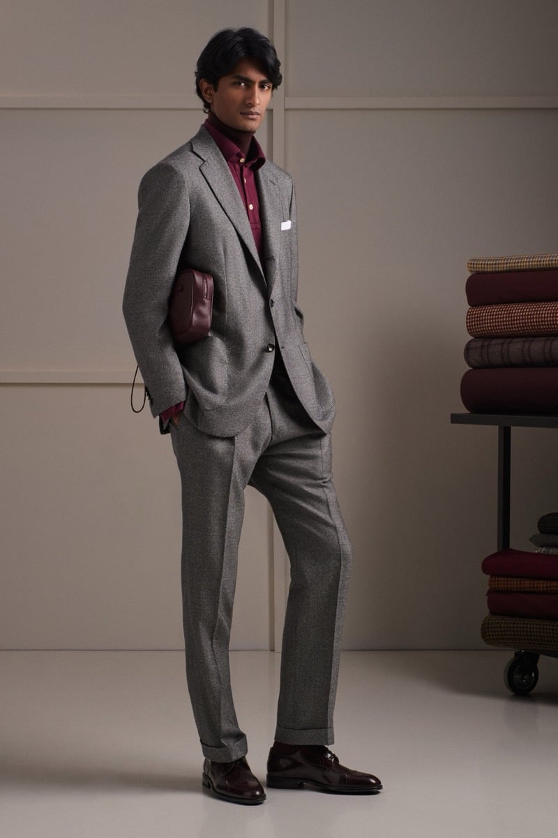 Rishi Robin wears a gray flannel three-piece suit over a burgundy shirt with a small burgundy leather bag