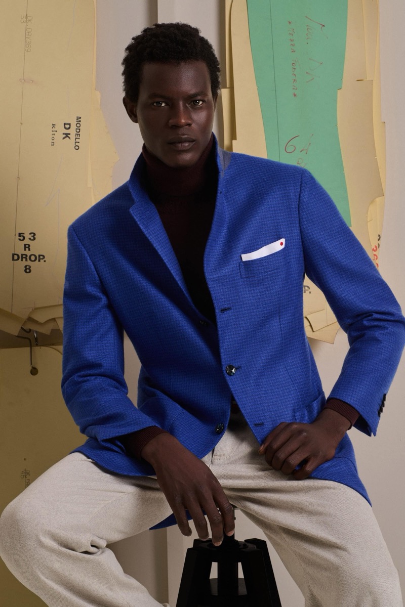 Mohammed Abubakar wears a royal blue stand-collar blazer with a white pocket square over a burgundy turtleneck and cream trousers