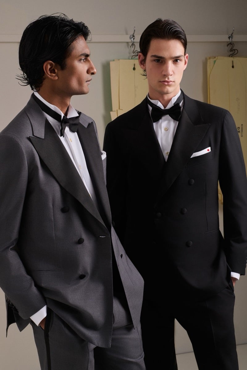 Rishi Robin wears a gray double-breasted peak-lapel tuxedo with a black bow tie beside Noah Herbst in a black double-breasted peak-lapel tuxedo with a black bow tie