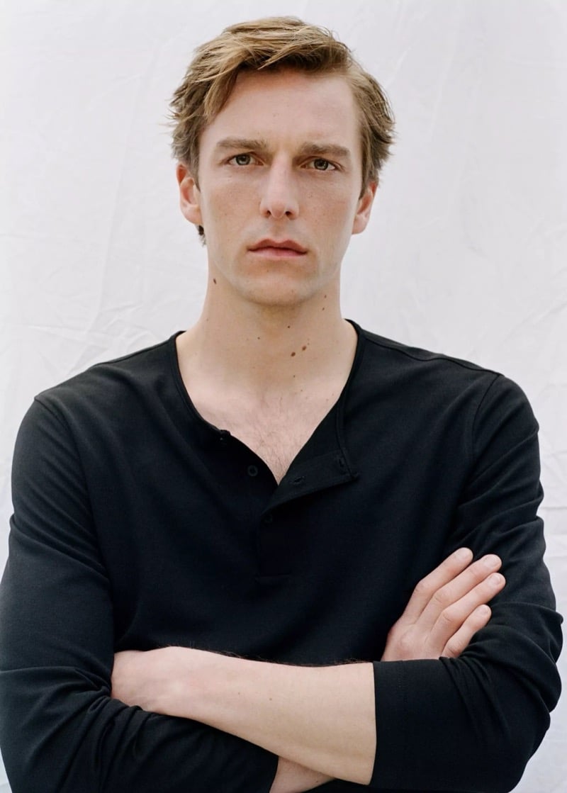 Quentin crosses his arms in a Mango black long-sleeve henley against a white backdrop