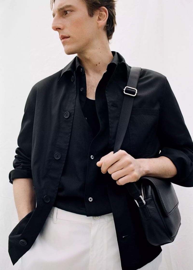 Quentin wears a Mango black linen overshirt over a black shirt with white trousers and a black leather crossbody bag