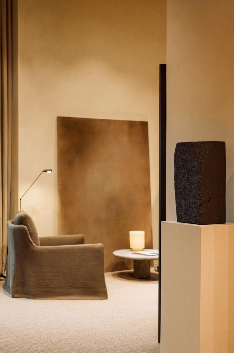 A linen slipcovered armchair and round marble side table sit beside a plaster wall and a dark textured sculpture on a pale plinth inside the Palma flagship