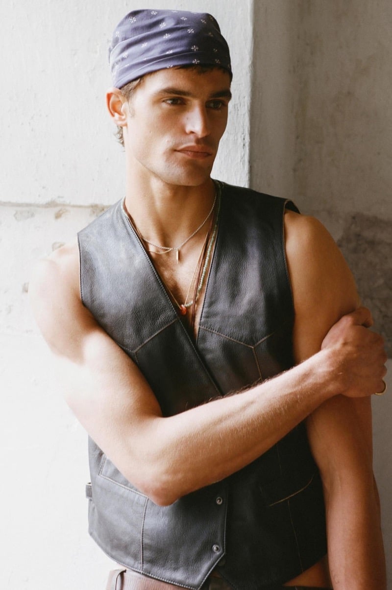 Parker wears a black leather vest on bare skin with a purple bandana and layered necklaces against a cracked plaster wall for Zara