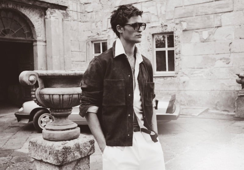 Parker wears a suede jacket over a white shirt with sunglasses in a stone courtyard with a convertible car for Zara