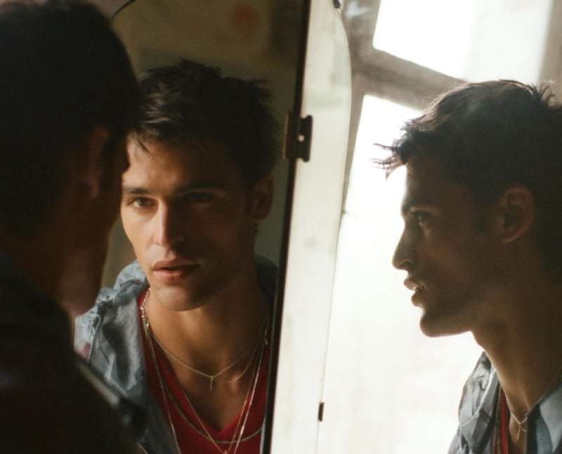 Parker gazes into a mirror wearing a red t-shirt under an open technical jacket with layered necklaces for Zara