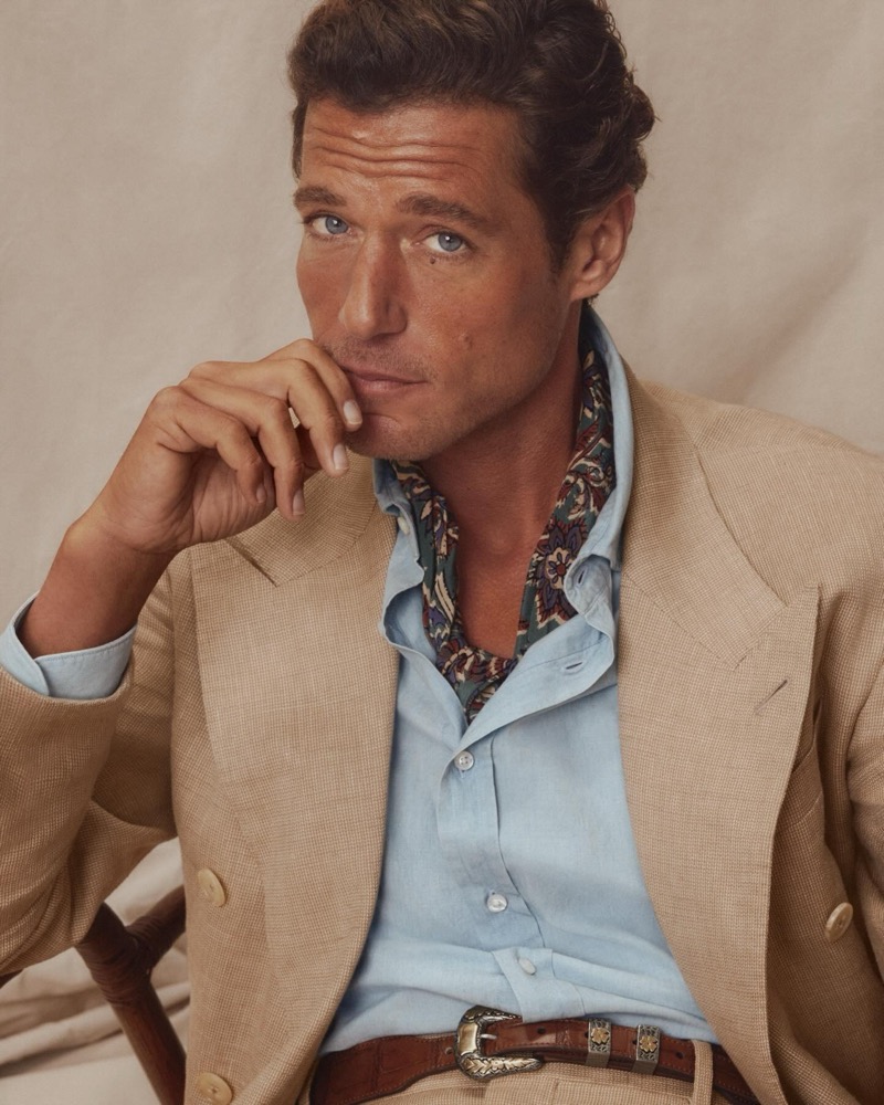 Close-up of Jon Paul in a tan linen suit with a light blue shirt, paisley silk neckerchief, and a Western belt with engraved silver buckle