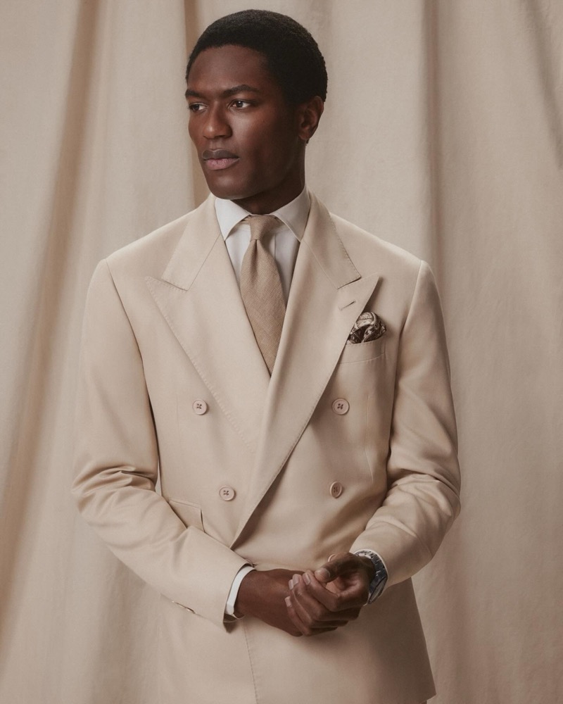 Hamid wears a champagne double-breasted peak-lapel suit with a white shirt, tan tie, and paisley pocket square