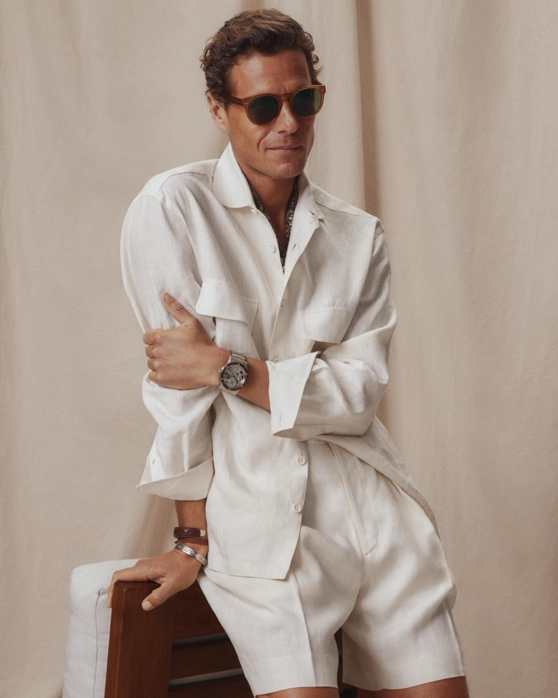 Jon Paul wears a cream linen camp-collar safari shirt with matching shorts, tortoiseshell sunglasses, and stacked silver and leather bracelets
