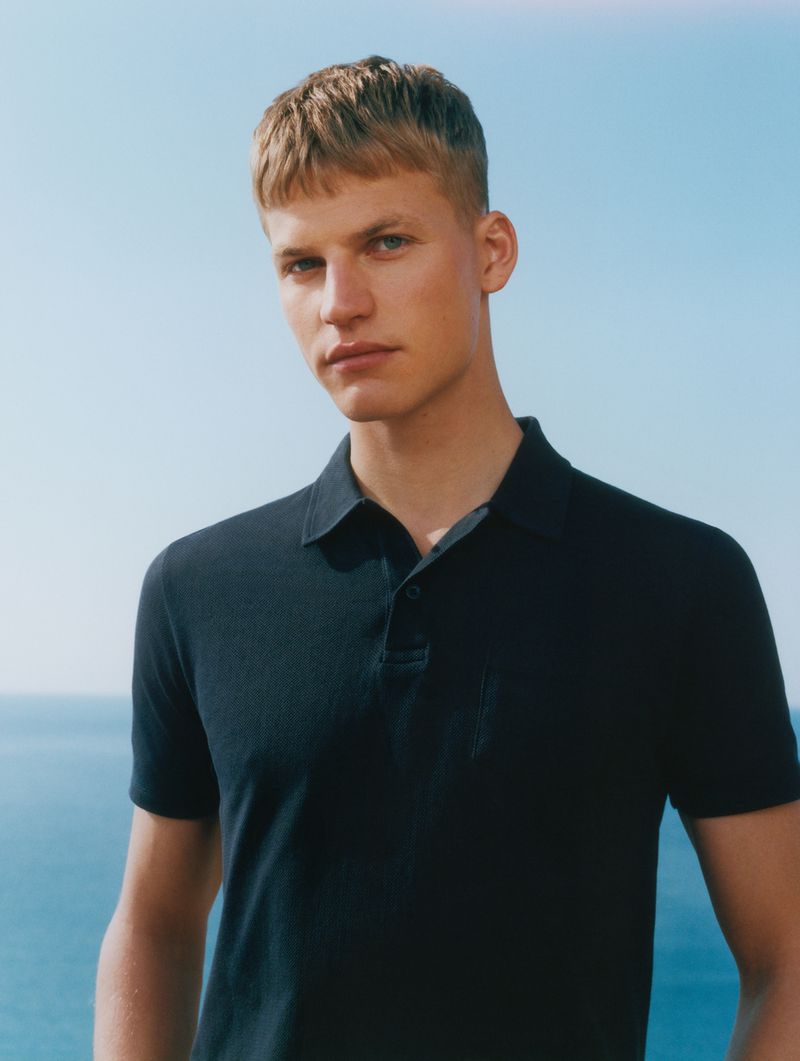 Timo stands against a sea and sky backdrop in a navy short-sleeve Riviera polo cut from textured cotton pique