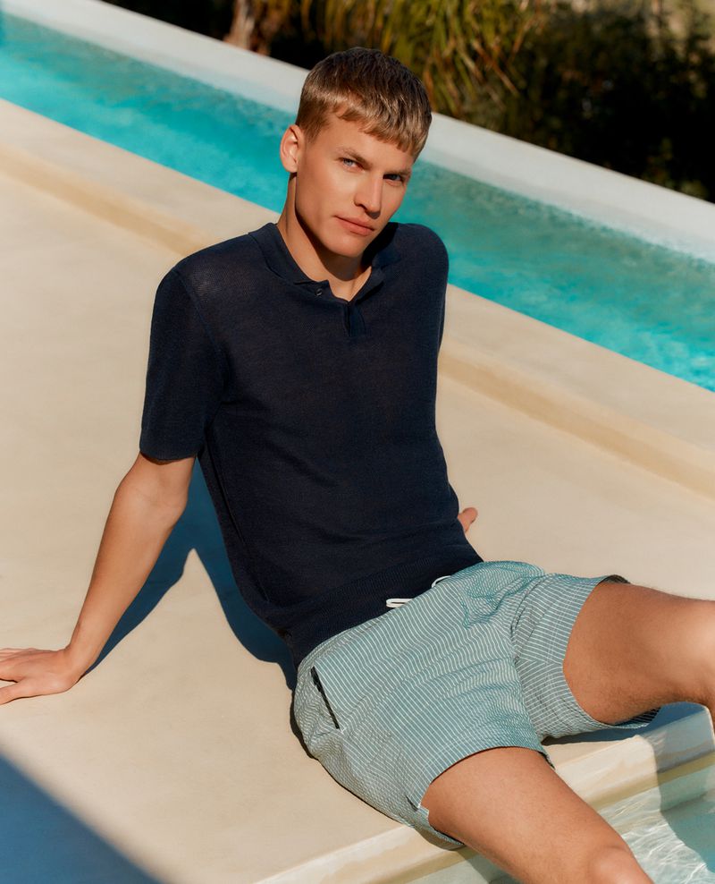 Timo sits poolside in a navy textured knit polo with pale green and white striped seersucker drawstring swim shorts