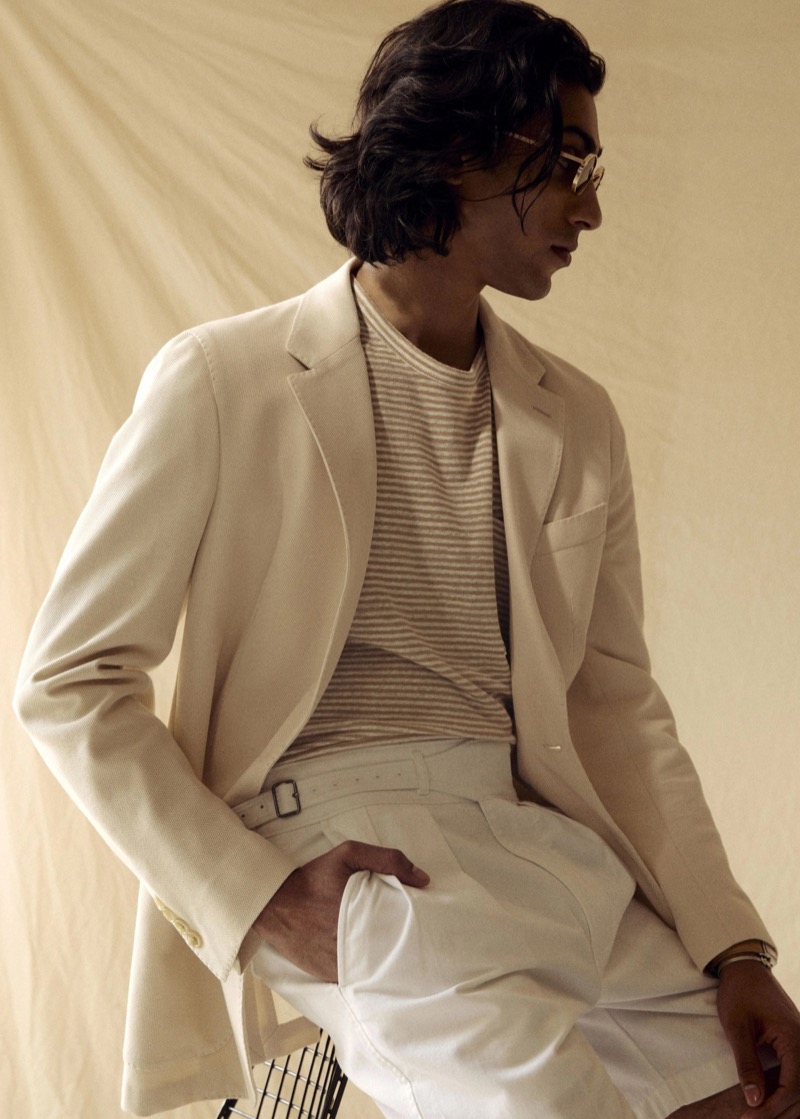 Adarsh wears a Todd Snyder Italian knit sport coat in birch over a tan and cream striped tee with white pleated Mylos linen shorts and gold-framed glasses