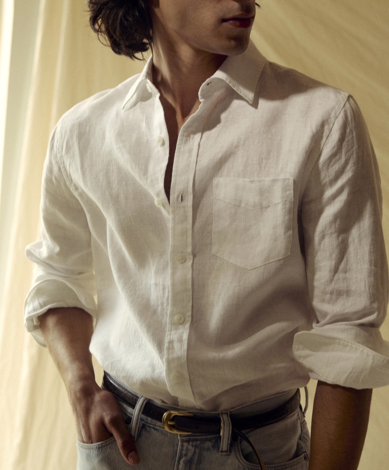 Adam wears a Todd Snyder Sea Soft white linen point-collar shirt with sleeves rolled, tucked into light wash denim with a brown leather belt and gold buckle
