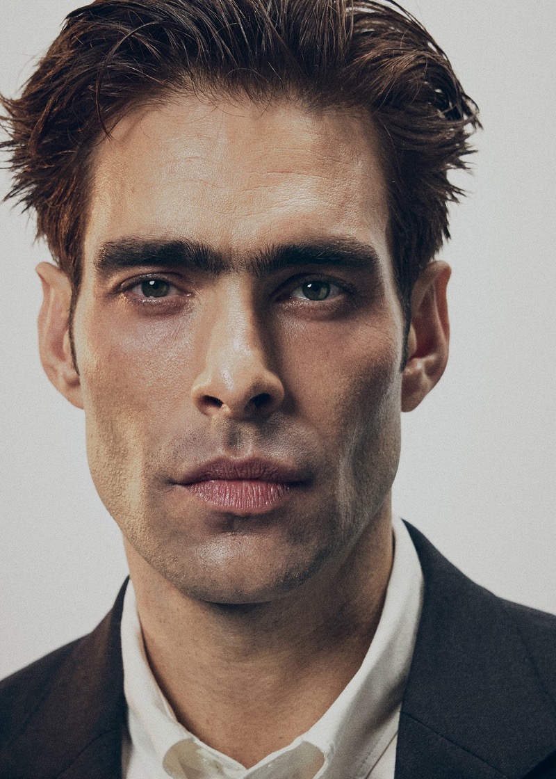 Tight portrait of Jon with wet, swept-back hair in a black blazer over an open white shirt