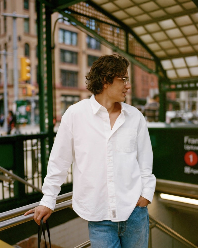 Model Tony Özkan heads into a New York subway station wearing the A&F oxford button-up shirt over washed blue jeans with clear-frame glasses