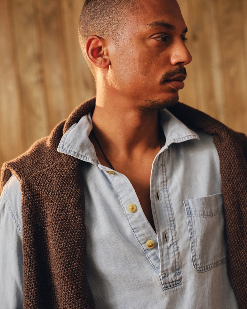 Side profile of Ysham Jackson in a light-wash Abercrombie & Fitch chambray denim popover with a brown crew sweater draped over his shoulder