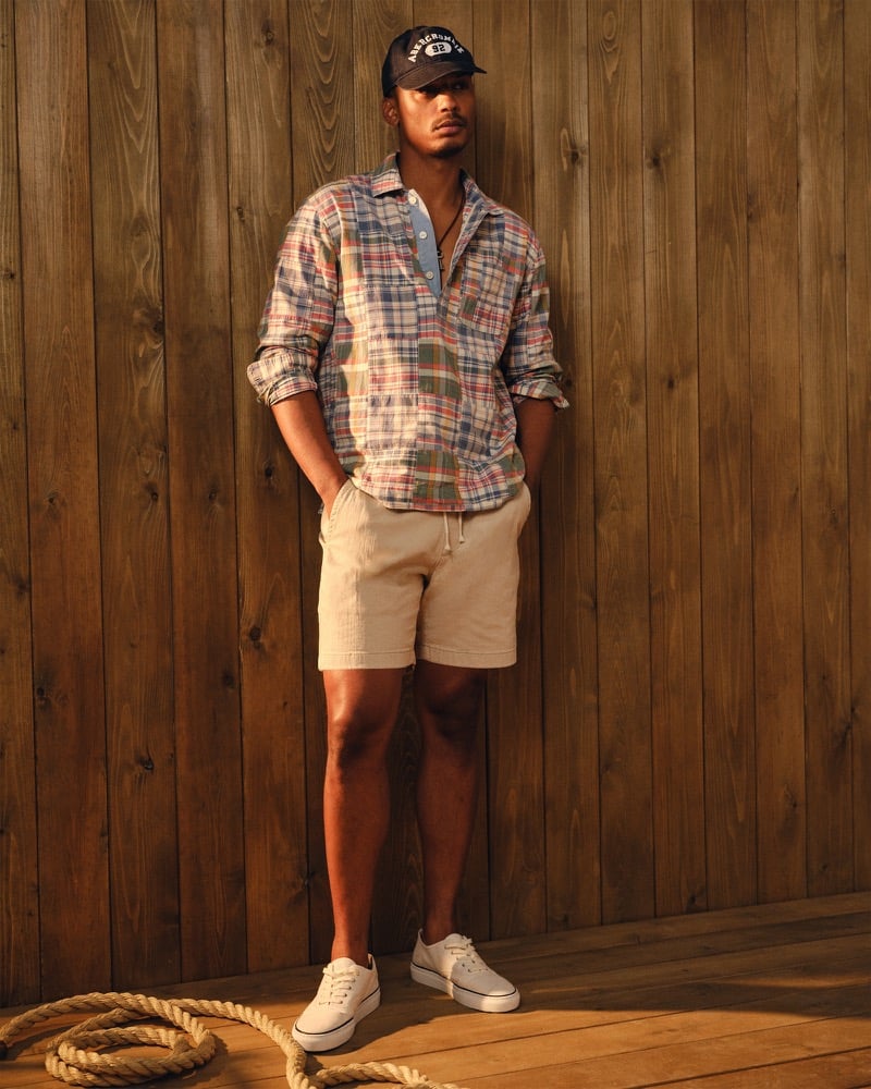 Ysham Jackson in a navy Abercrombie baseball cap, the patchwork madras Abercrombie & Fitch popover shirt over a chambray placket, tan drawstring shorts, and white canvas sneakers
