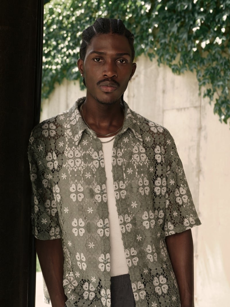 Anarcius Jean wears an olive green floral lace short-sleeve camp shirt over a white tank with silver chains