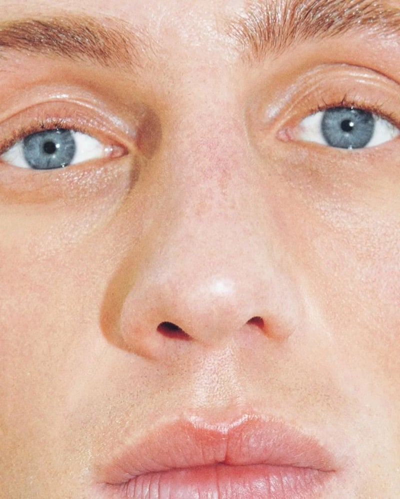 Extreme close-up of Aubrey O'Mahony's face from brow to chin, showing his pale blue eyes, freckled skin, and pink lips