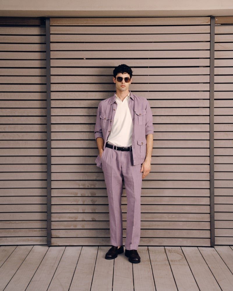 Model Alessandro Rengo in round tortoise sunglasses, a faded lavender linen utility shirt-jacket and matching pleated trousers over a white polo with a black belt and dark brown loafers