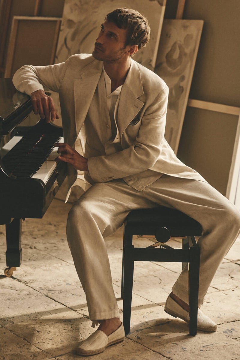 Clément Chabernaud rests at a grand piano in a stone-toned linen single-breasted suit and matching vest, finished with sand espadrille loafers, inside a sunlit Sicilian studio