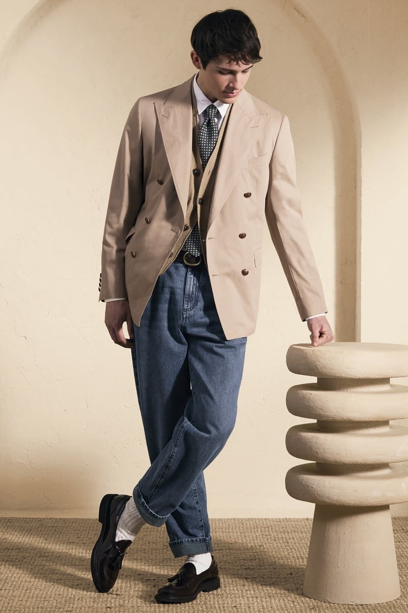 Model Mateo Ruiz in a cream double-breasted blazer over a tan knit cardigan and white shirt with a navy polka-dot tie, paired with blue washed jeans and dark brown tassel loafers