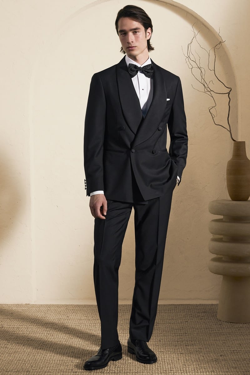 Model Peter Meyer in a black double-breasted shawl-collar tuxedo over a white pleated tuxedo shirt and black silk bow tie, finished with black leather loafers