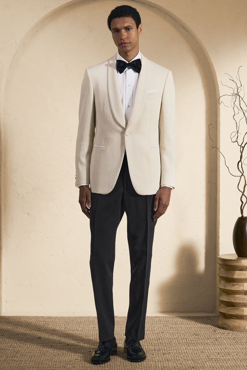 Model Gilbert van Damme in an ivory shawl-collar dinner jacket over a white pleated tuxedo shirt and black silk bow tie, paired with black trousers and black tassel loafers