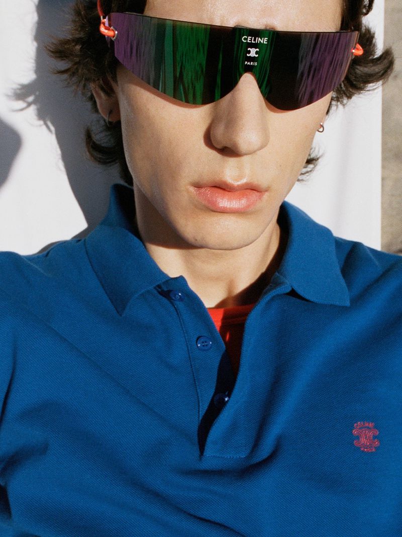 Samuel Funs wears Celine futuristic shield sunglasses with mirrored green lenses and a blue piqué polo embroidered with the Celine crest
