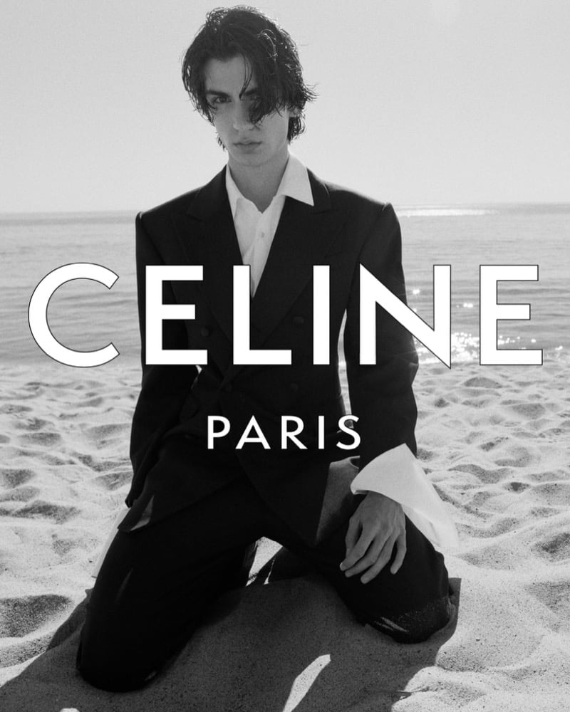 Samuel Funs kneels barefoot in the sand wearing a double-breasted suit and open-collar dress shirt, with the Celine Paris logo overlaid on the horizon