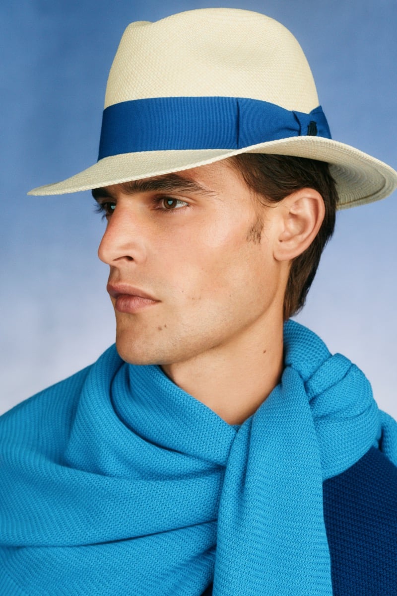 Model Parker Van Noord in a cream Panama hat with a blue band, draped in a turquoise knit scarf