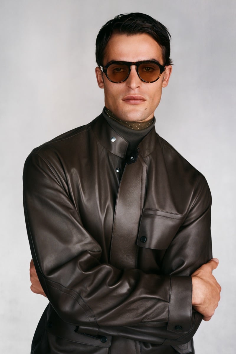 Model Parker Van Noord in tortoise round sunglasses wears a dark brown leather shirt jacket over an olive turtleneck and printed olive neckerchief