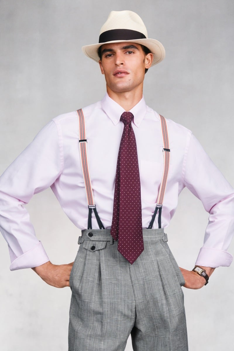 Model Parker Van Noord in a cream Panama hat with a brown band wears a pale pink button-down shirt with a burgundy polka-dot tie and orange-and-cream striped suspenders, paired with gray Prince of Wales check pleated trousers