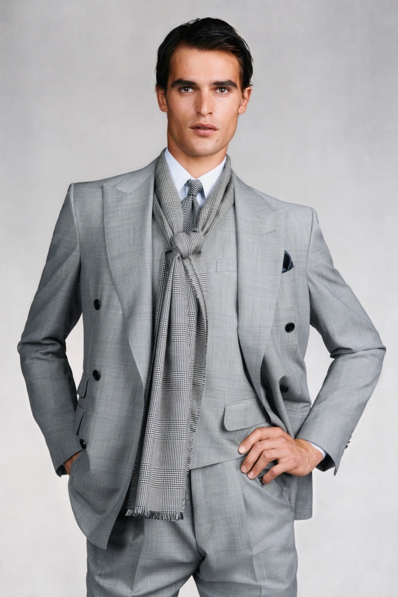 Model Parker Van Noord in a gray Prince of Wales check three-piece suit with peak lapels and matching vest wears a pale blue shirt with a houndstooth tie and matching long houndstooth scarf knotted at the chest