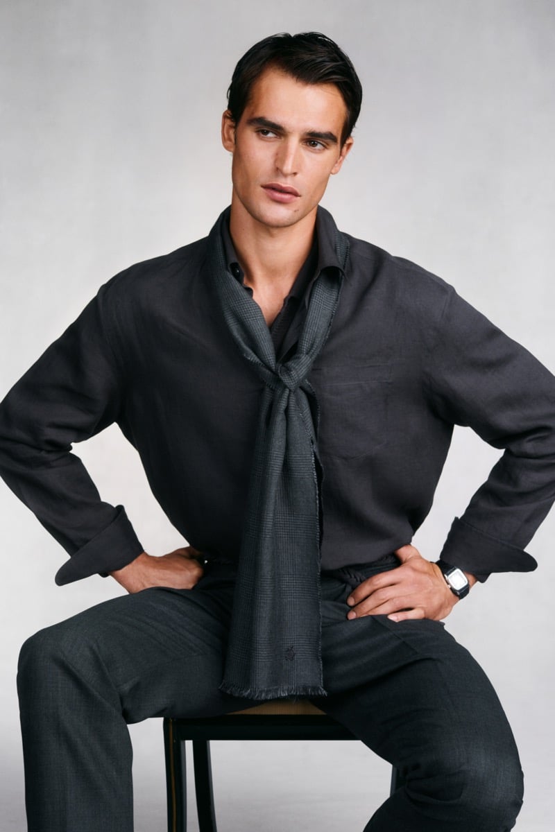 Model Parker Van Noord sits on a stool in a charcoal linen shirt and matching trousers with a Prince of Wales check scarf knotted at the chest