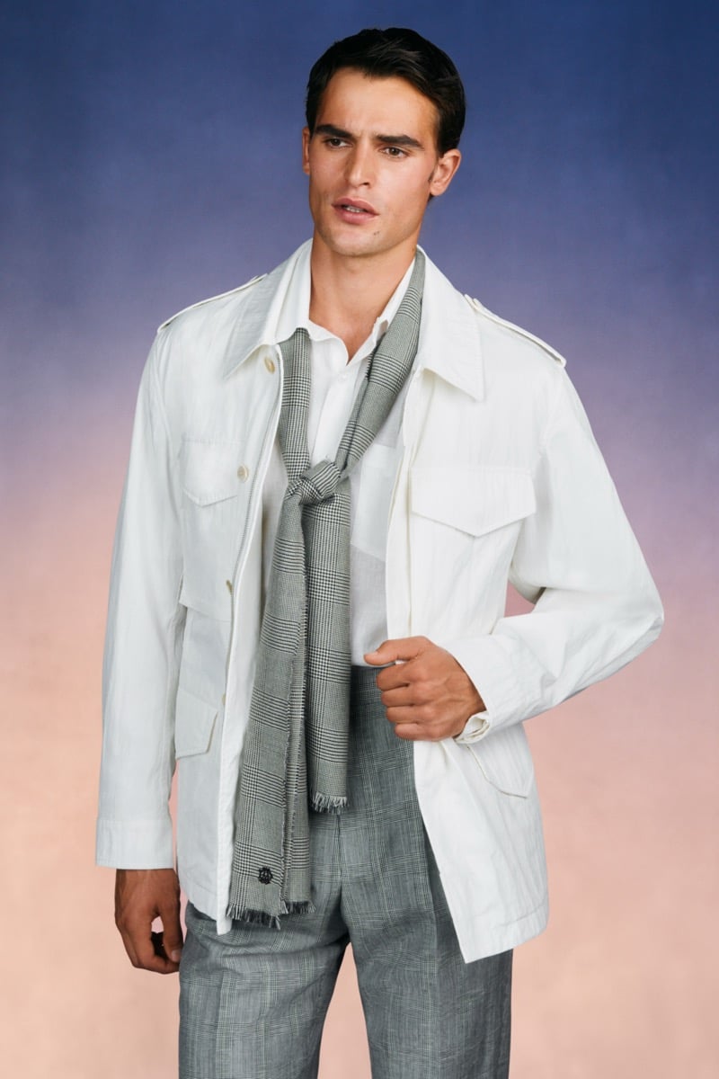 Model Parker Van Noord in a cream cotton field jacket with four utility pockets over a white shirt and Prince of Wales check scarf, paired with gray check trousers