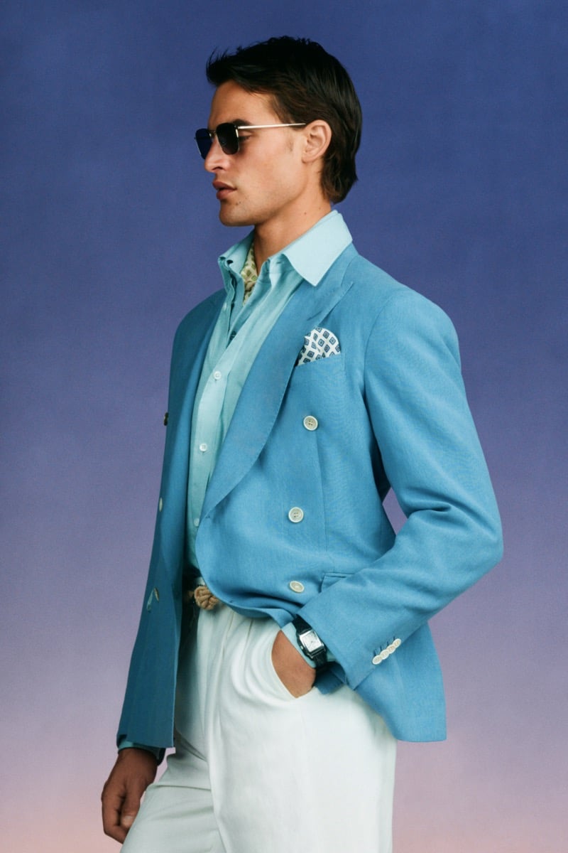 Model Parker Van Noord in aviator sunglasses wears a turquoise double-breasted linen blazer with a printed pocket square over a mint shirt and printed scarf, finished with a woven rope belt and white trousers