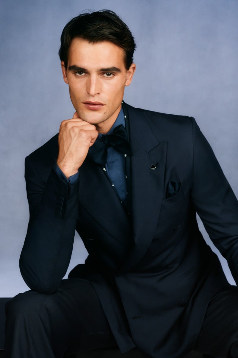 Model Parker Van Noord in a navy peak-lapel tuxedo jacket with a spade lapel pin over a navy polka-dot shirt and black silk bow tie