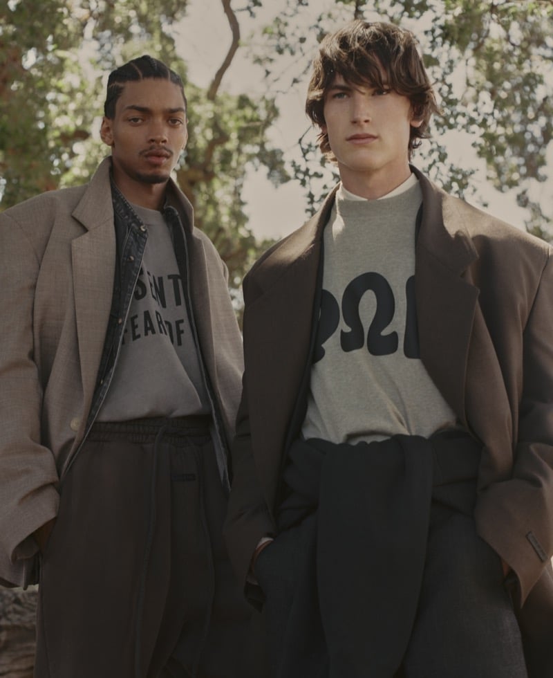 Omari Phipps and Sean Linden wear oversized earth-toned blazers layered over heather Fear of God graphic crewnecks with relaxed trousers under oak trees