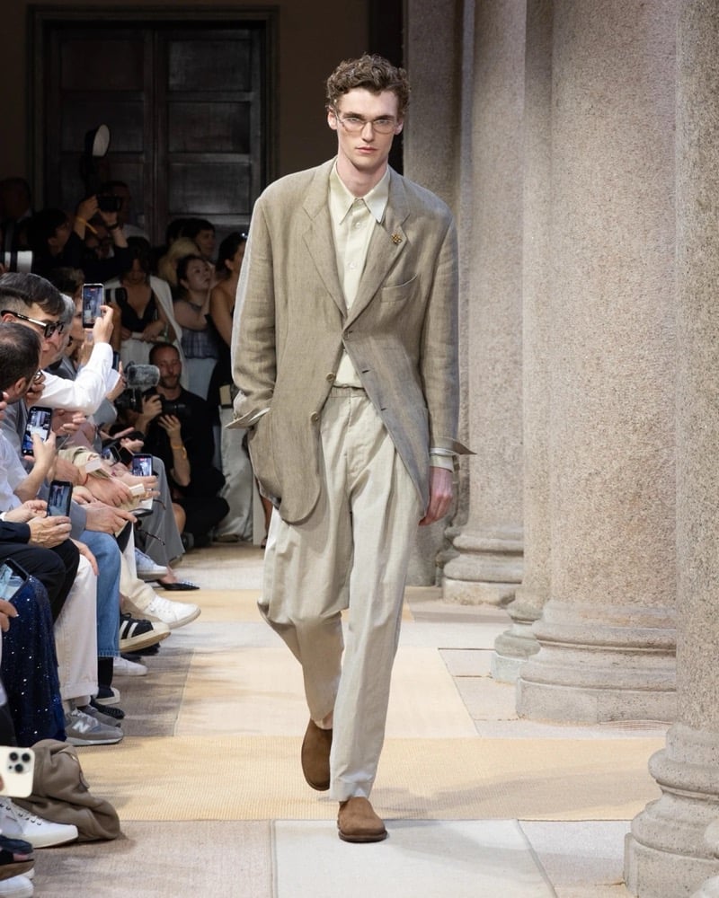 Model wears an elongated single-breasted linen blazer with notch lapels over a tonal shirt and matching wide pleated linen trousers