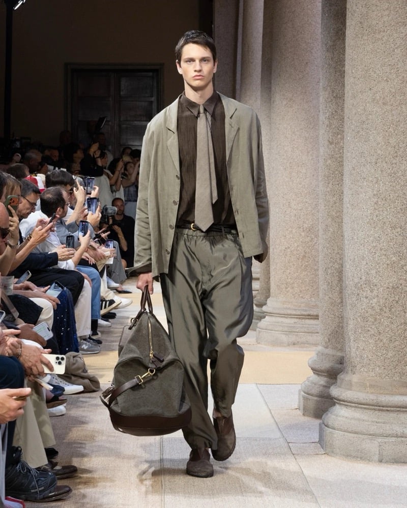 Model wears an oversized linen blazer over a soft shirt with a long knitted tie, paired with wide pleated silk trousers