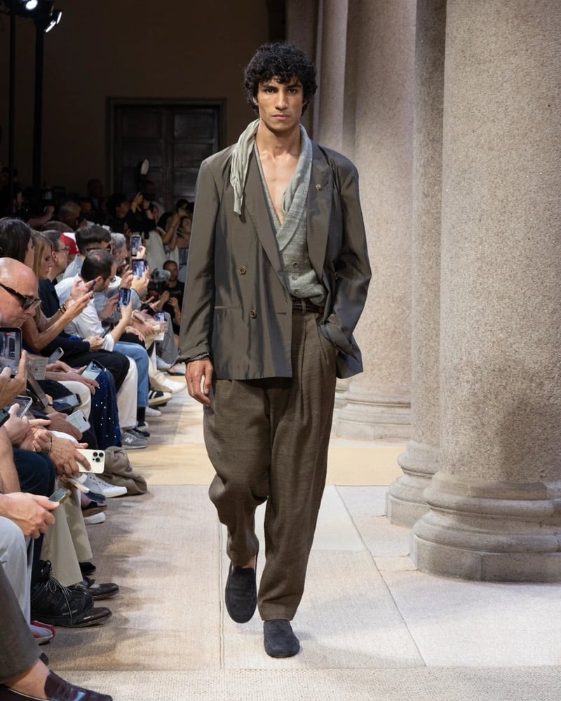 Model wears a double-breasted shawl-collar linen jacket layered over a draped knit and a soft scarf, paired with wide pleated linen trousers