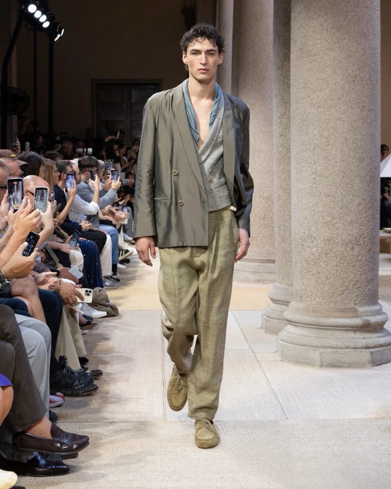 Model wears a double-breasted silk-blend jacket over a draped shawl-collar knit and a soft scarf, paired with wide pleated linen trousers