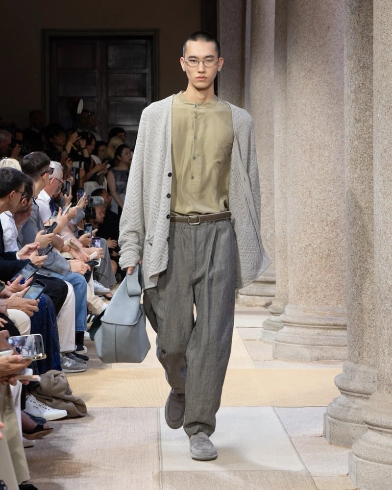 Model wears an oversized chevron-knit cardigan over a band-collar henley, paired with wide pleated linen trousers