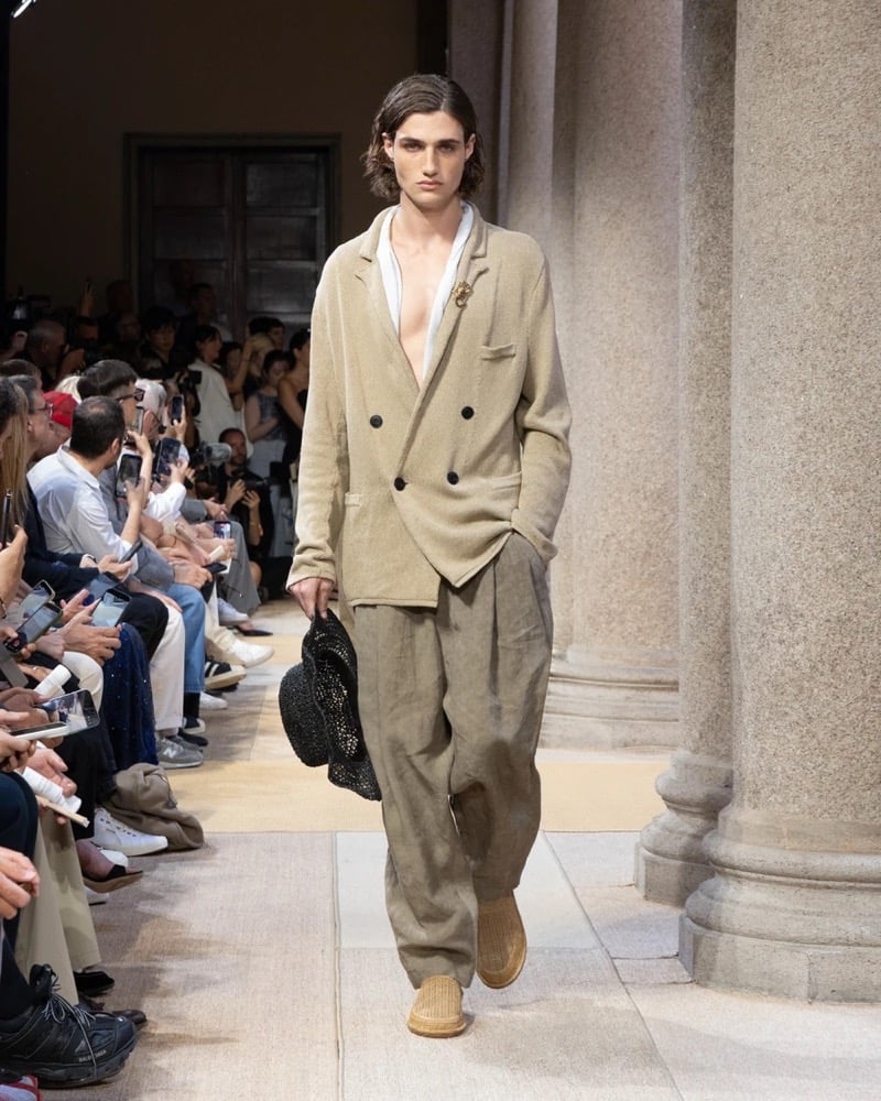 Model wears a double-breasted textured-linen jacket with patch pockets over an open shirt, paired with wide pleated drawstring linen trousers
