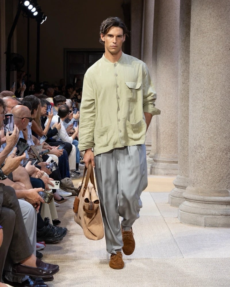 Model wears a relaxed band-collar linen shirt-jacket with a chest flap pocket and patch pockets, paired with wide pleated silk trousers