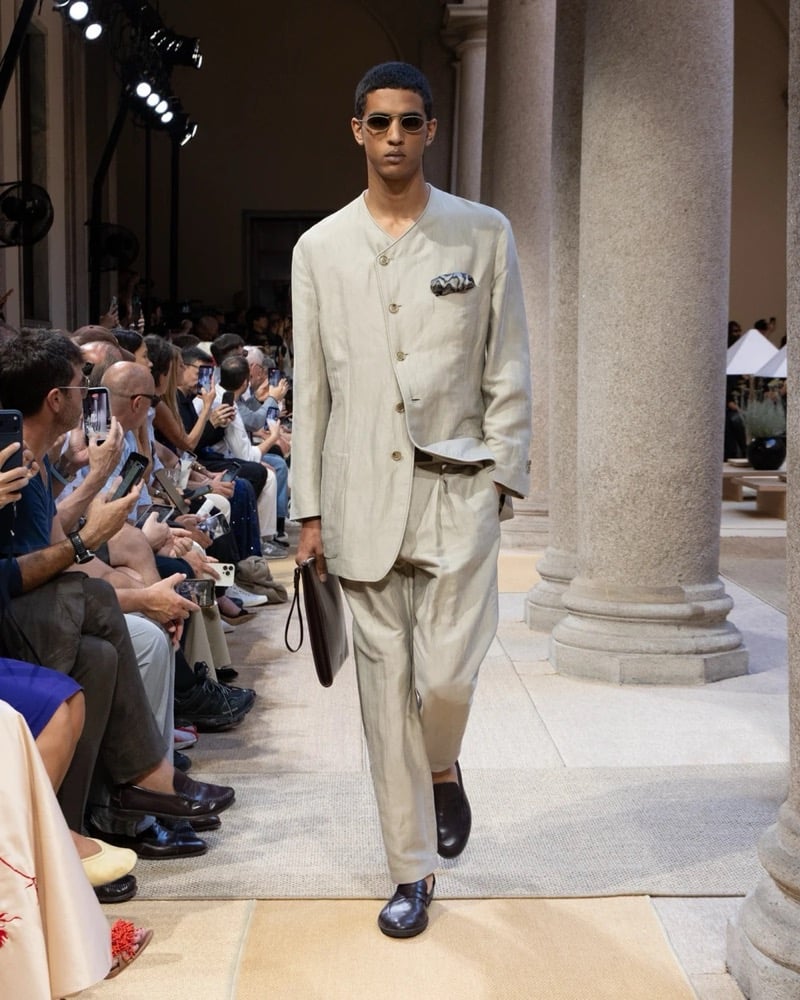 Model wears a band-collar linen jacket layered over a matching waistcoat and worn with wide pleated drawstring linen trousers