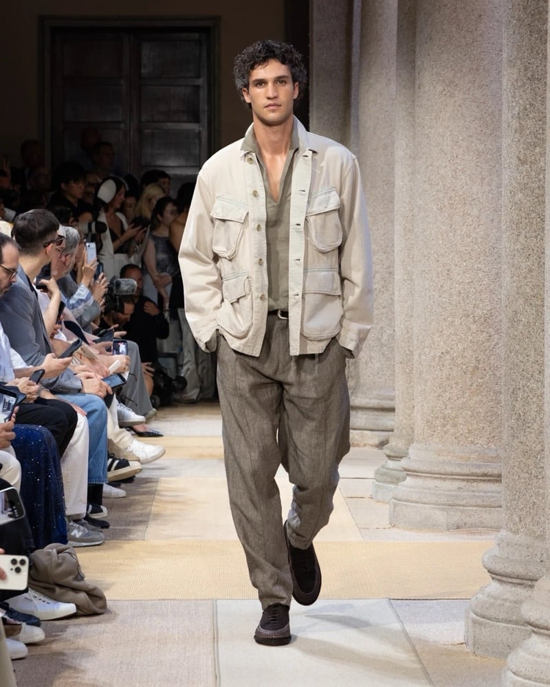 Model wears a utility-pocketed linen overshirt with chest flap pockets, layered over an open shirt and worn with wide pleated linen trousers