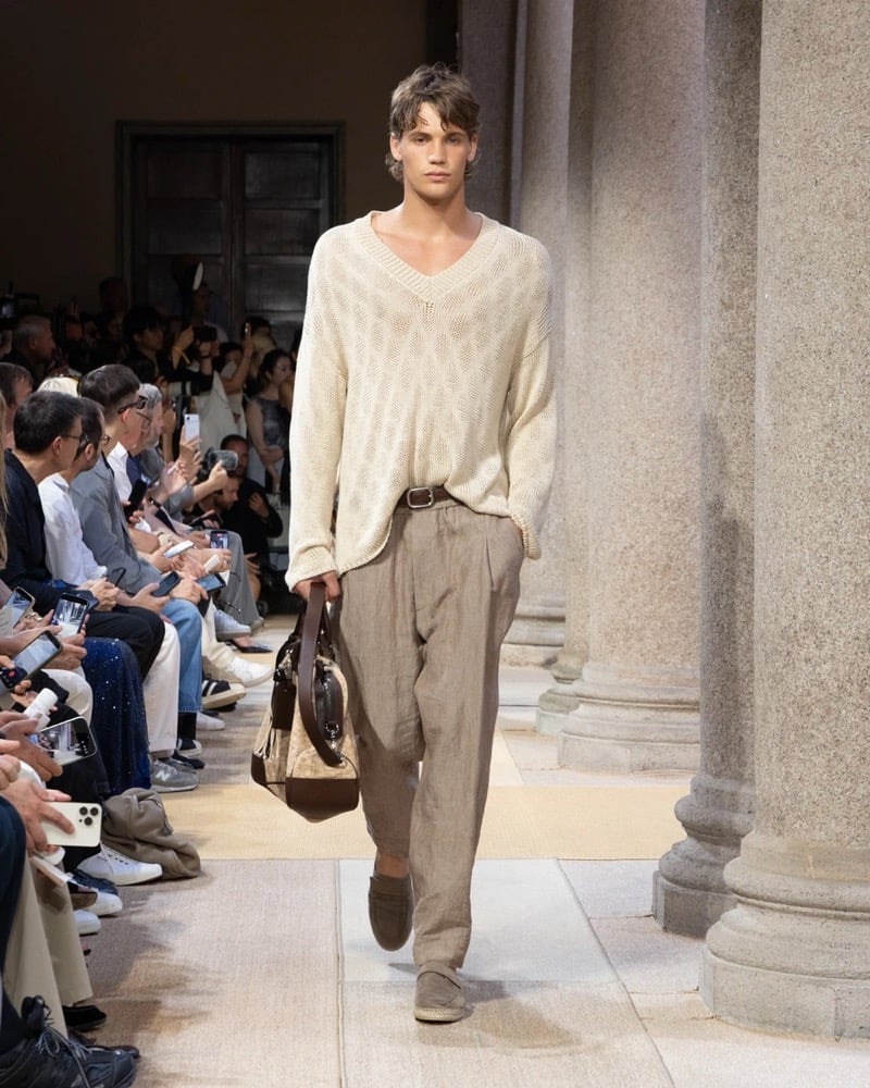 Model wears an oversized open-knit long-sleeve V-neck pullover paired with wide pleated linen trousers
