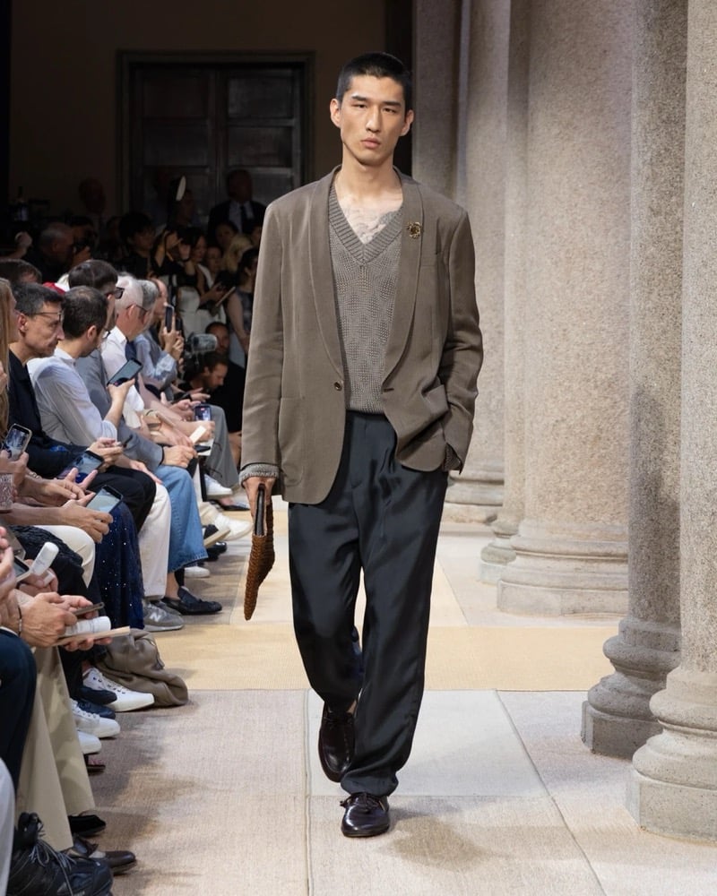 Model wears a relaxed single-button linen blazer over an open-knit V-neck pullover and lace top, paired with wide pleated silk trousers